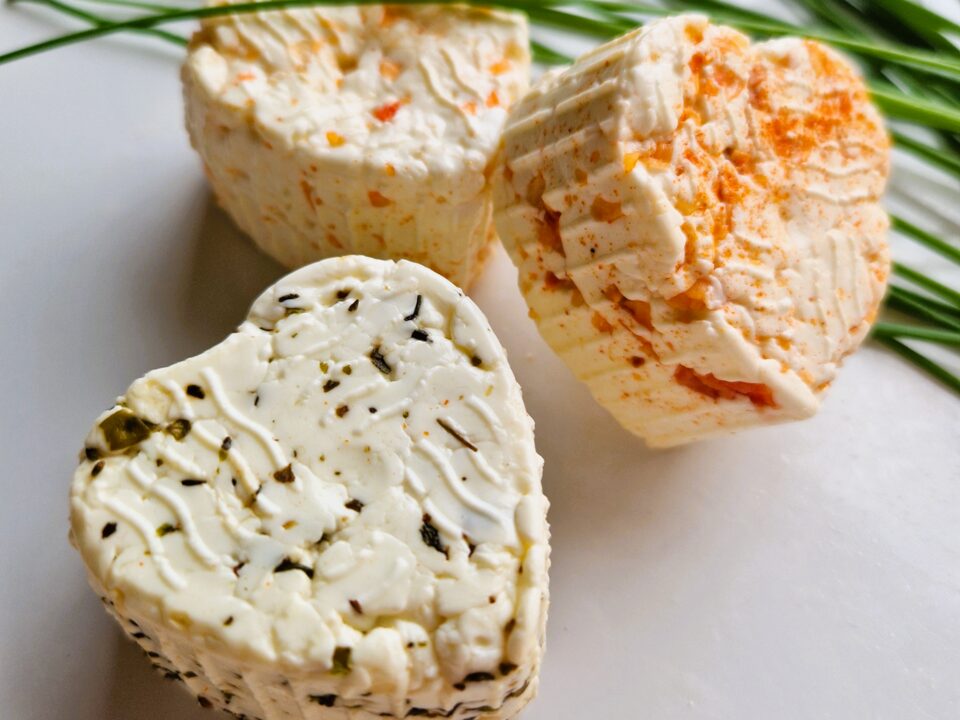 Tři čerstvé sýry ve tvaru srdce — s bylinkami, s paprikou a přírodní — na bílém talíři